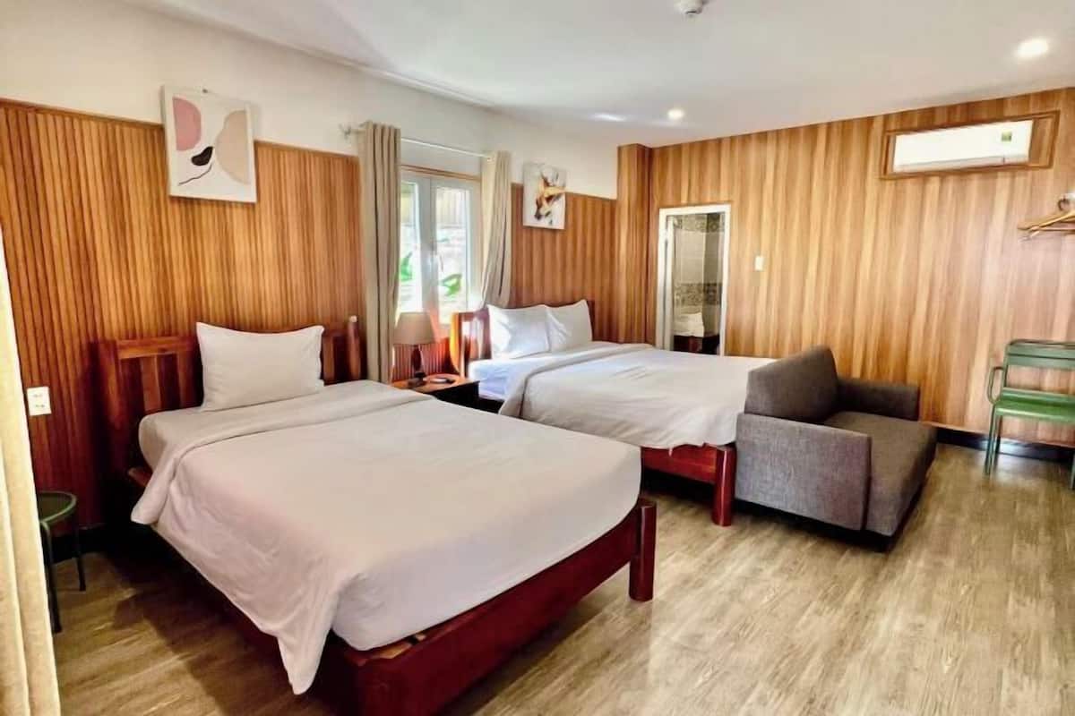 A hotel room with two beds, a sofa, wooden walls, and a window.