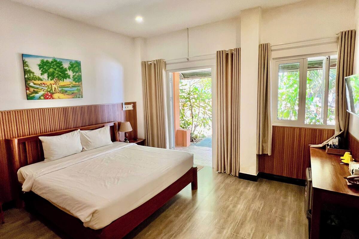 A hotel room with a bed, a desk, a television, and a painting on the wall.