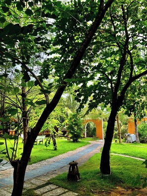 A pathway leading through a lush garden with trees and a small white bench. - Vida Loca Resort & Sunset Beach (Phu Quoc)