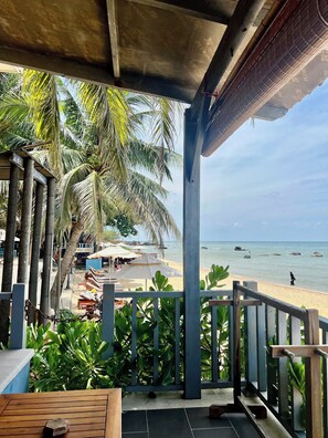 A beach view from a covered area with palm trees and a wooden deck. - Vida Loca Resort & Sunset Beach (Phu Quoc)