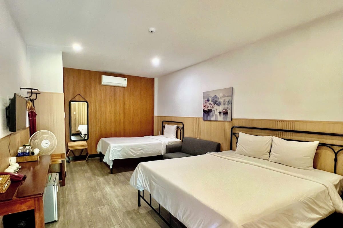 A hotel room with two beds, a desk, a chair, a mirror, and a painting on the wall.