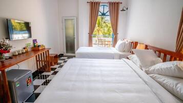Ein Hotelzimmer mit zwei Betten, einem Schreibtisch mit Computer, einem Fernseher und einem Balkon mit Vorhängen.