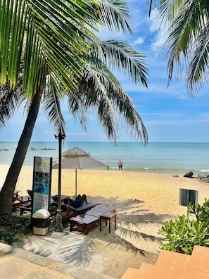 Una spiaggia con palme, un cartello, sdraio e un'area barbecue.