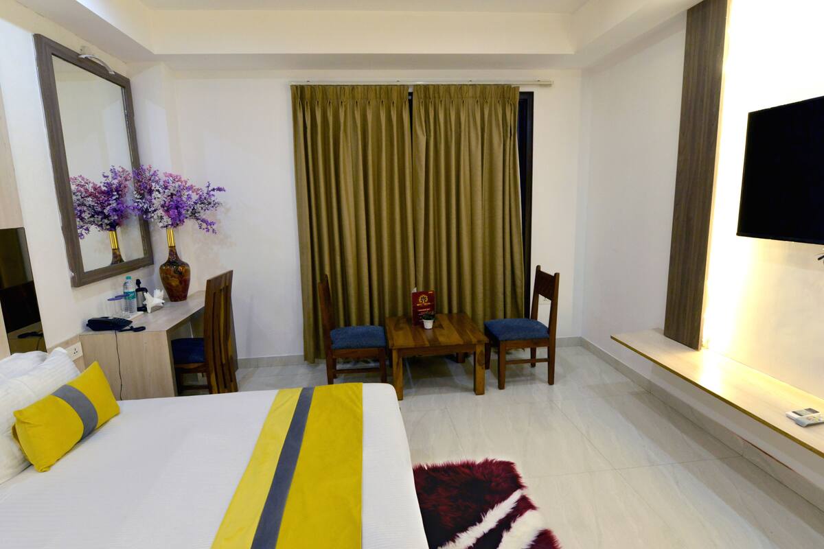 Habitación de hotel con cama, escritorio, dos sillas, televisión y ventana con cortinas.