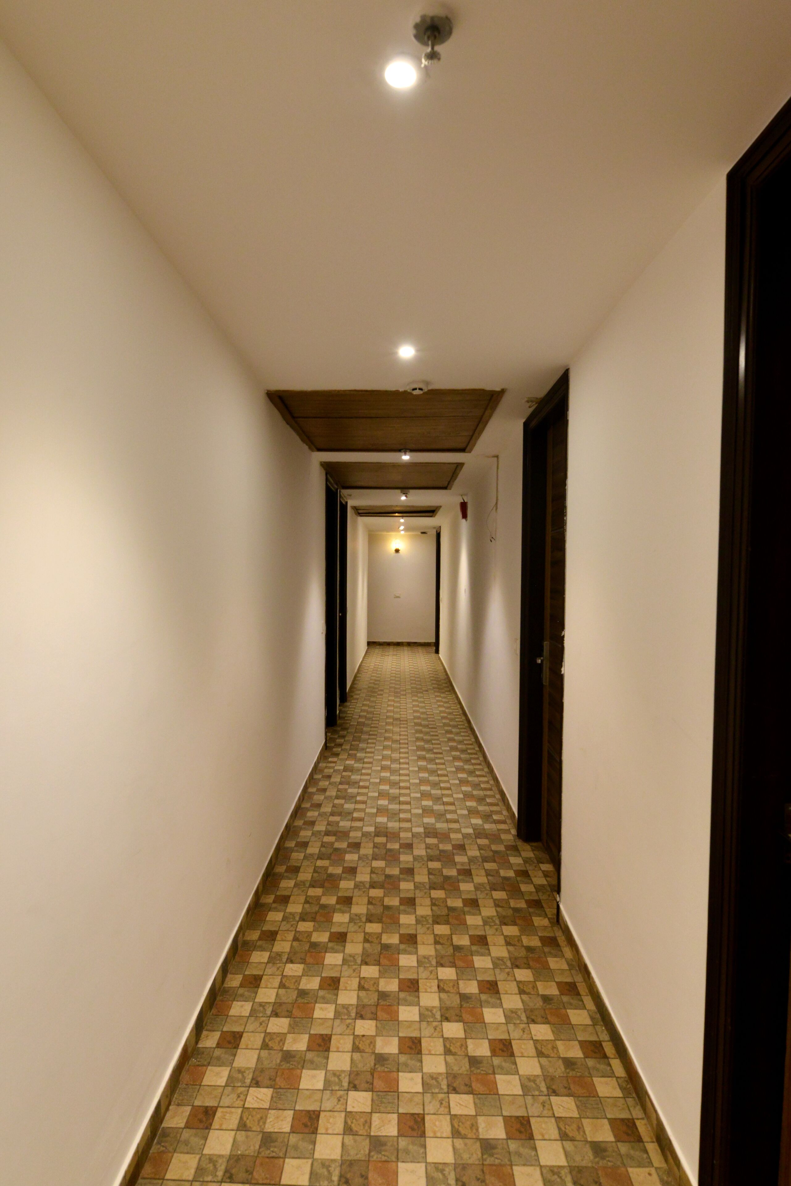 A narrow hallway with a checkered floor, white walls, and wooden ceiling beams.