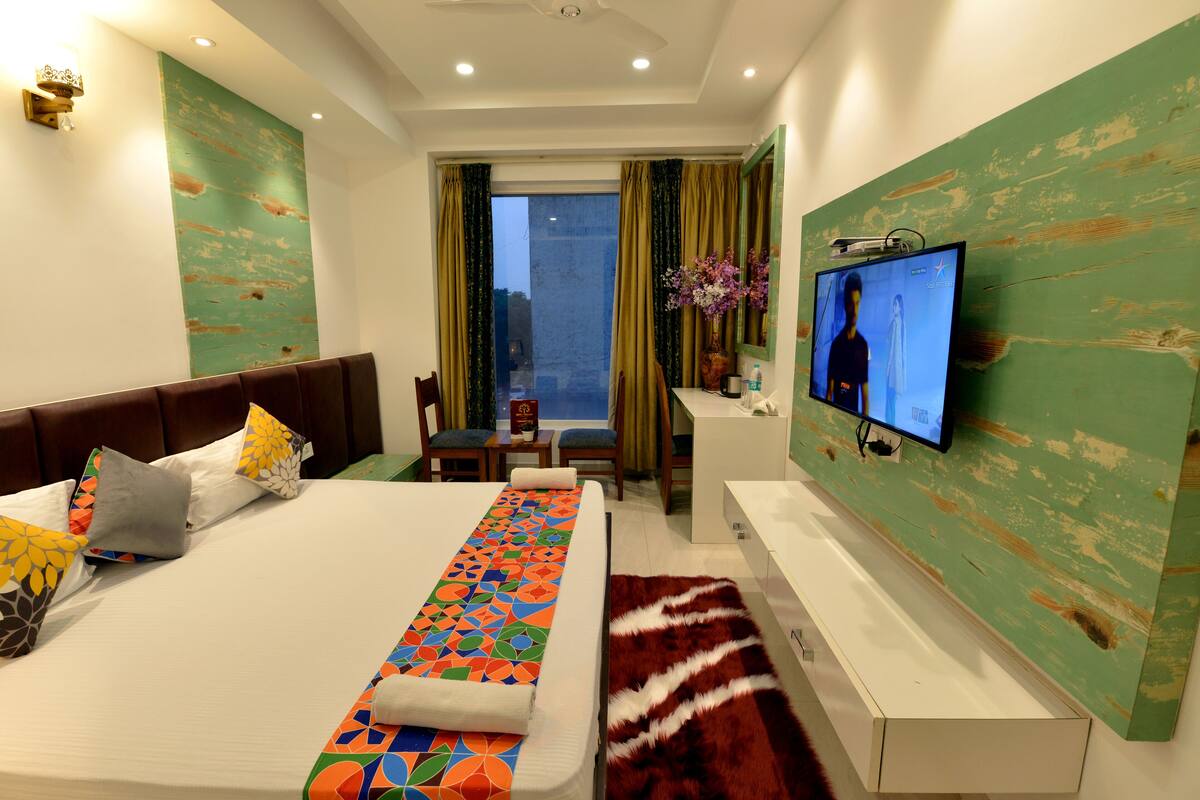 Habitación de hotel con una cama grande, televisión, escritorio y vista a la ciudad.
