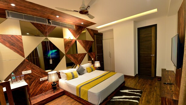 A modern bedroom with a wooden headboard, a bed with a striped bedspread, a bedside table with a lamp, and a large mirror on the wall.