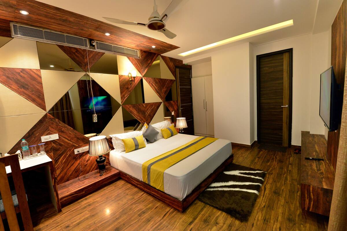 Un dormitorio moderno con cabecera de madera, cama con colcha a rayas, mesita de noche con lámpara y un espejo grande en la pared.