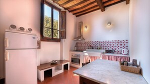 Cocina compacta con refrigerador, horno y ventana con vistas a árboles.