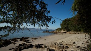 A beach with rocky terrain, clear water, and distant mountains. - Hotel A Maquía (Poio)
