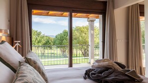 A bedroom with a large bed, a view of a green landscape through a sliding door, and a balcony with a railing. - Hotel A Maquía (Poio)