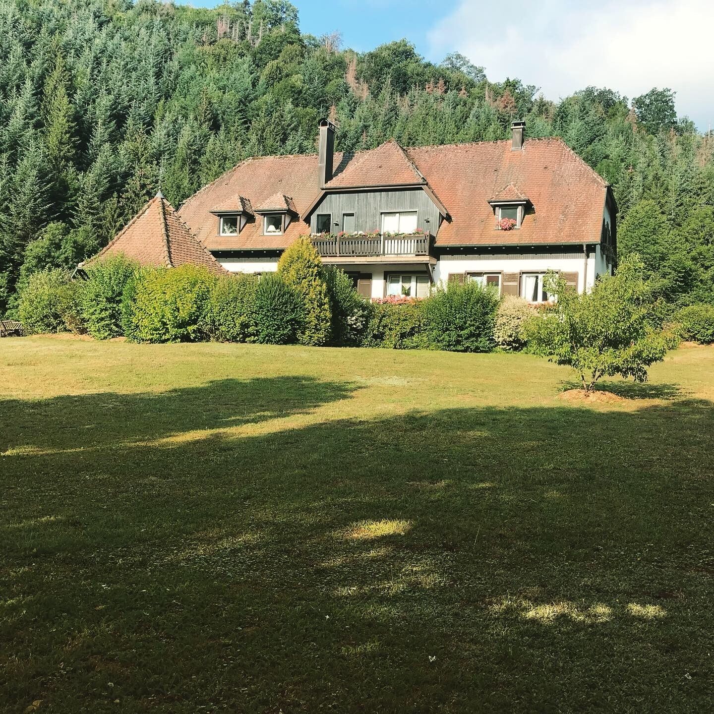 A two-story house with a sloped roof, a balcony on the upper floor, and a well-maintained lawn in front.