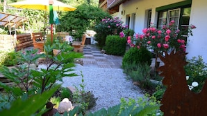 A garden with a wooden deck, a yellow umbrella, and pink flowers. - Weingut Seiner vlg. Kraxner (Sankt Stefan ob Stainz)