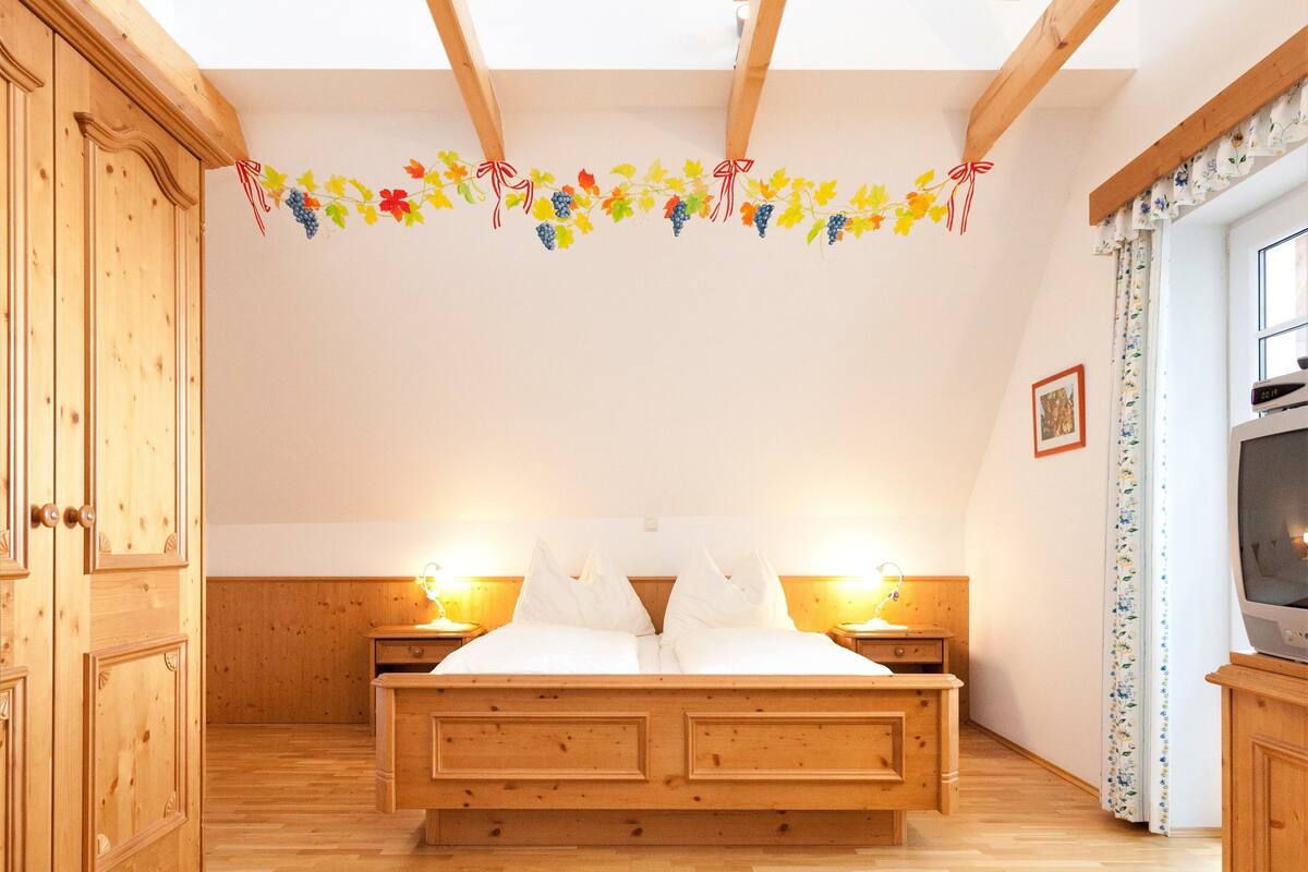 A bedroom with a wooden bed, wooden wardrobe, and a television on a cabinet.