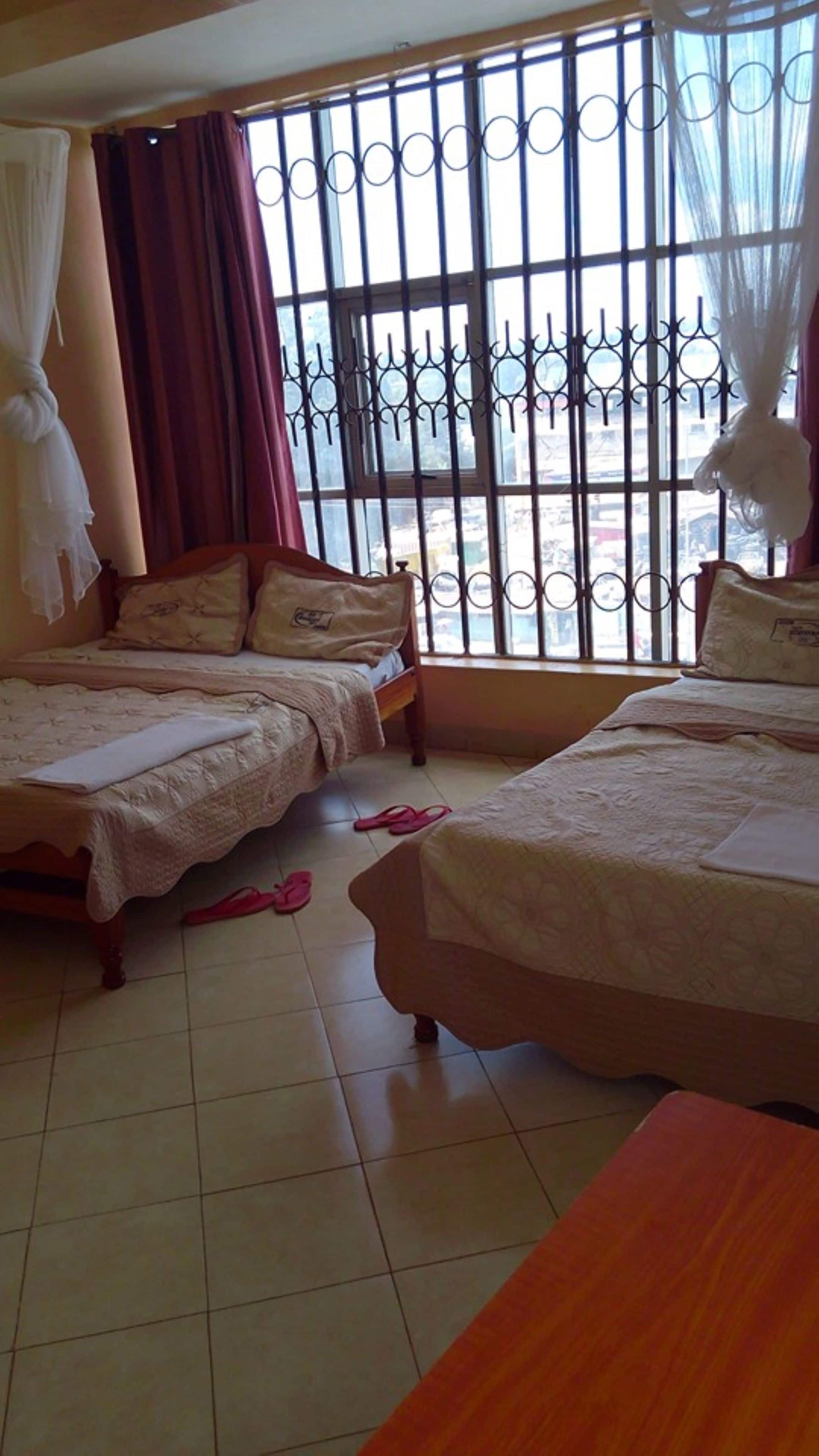 A room with two beds, a window with metal bars, and a curtain.