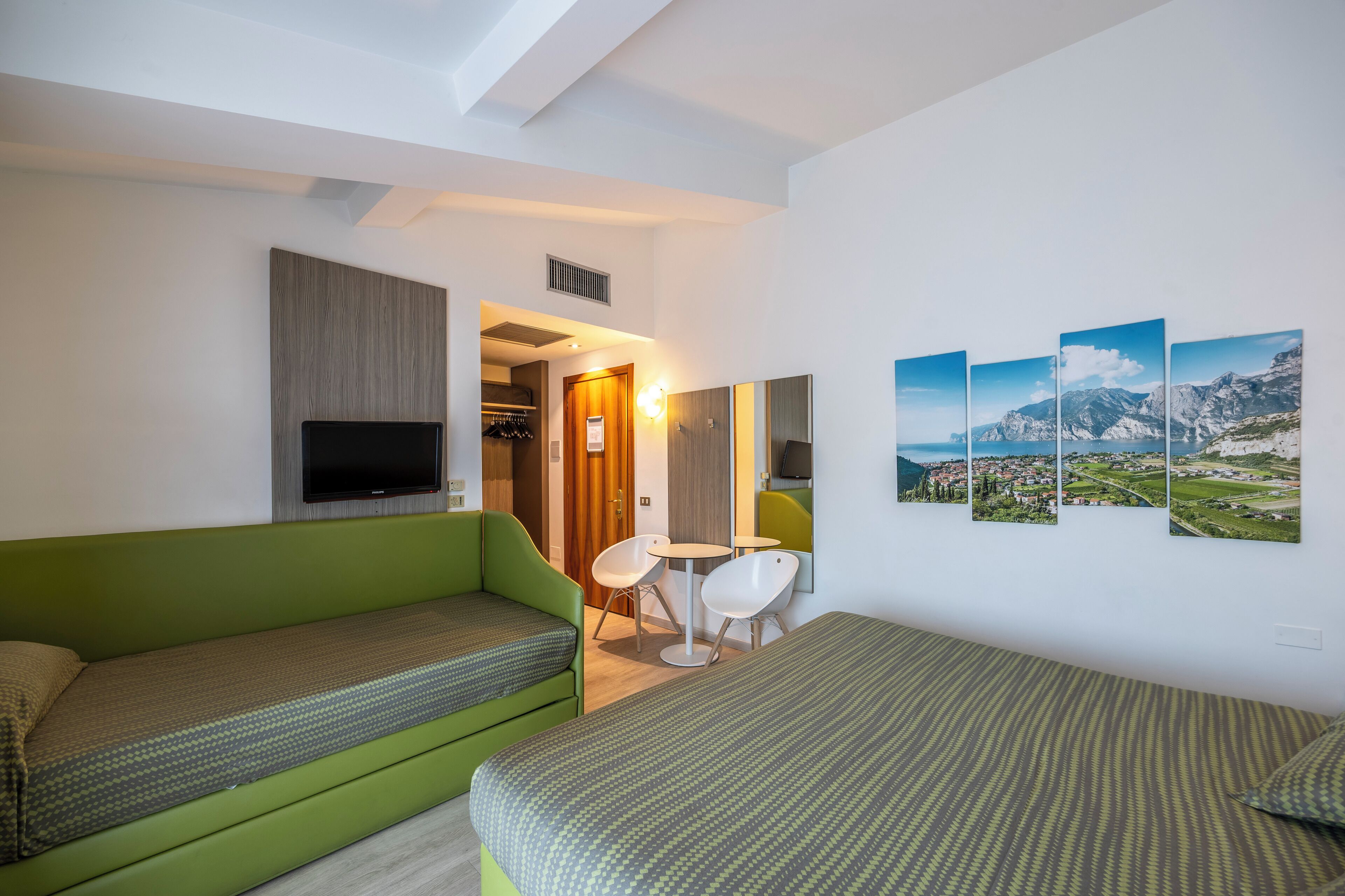 Una habitación de hotel moderna con un sofá verde, una cama, una mesita y un televisor.