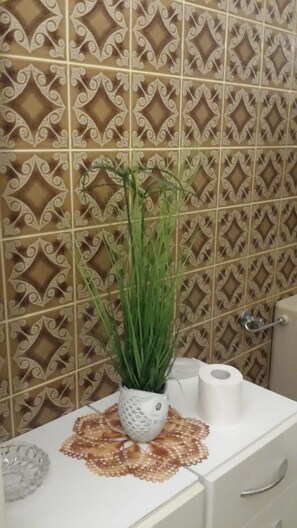 A bathroom with patterned tiles, a potted plant, a toilet paper roll, and a decorative doily on the counter. - Zum Altbreitenfelder Hof (Homburg)