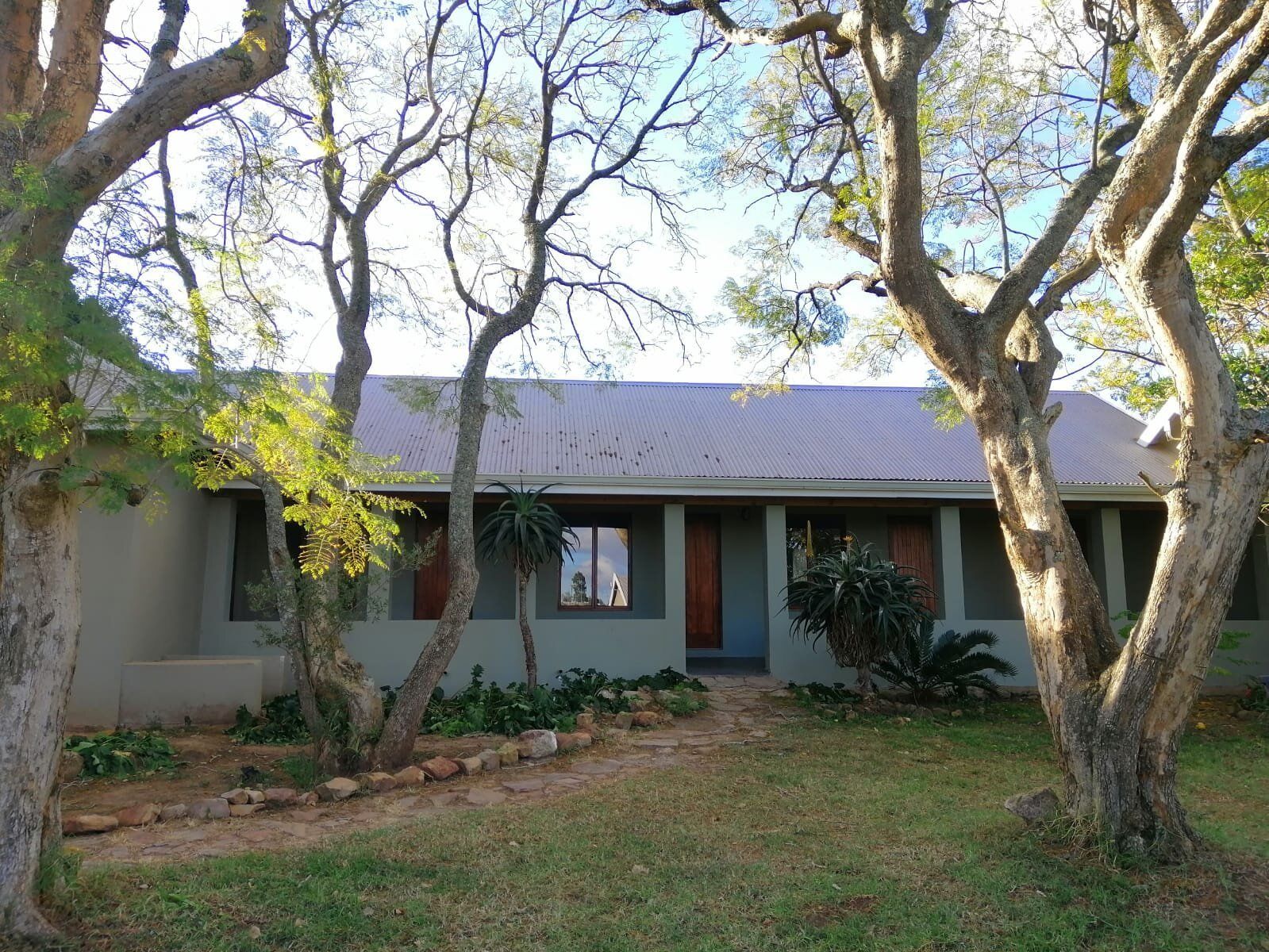 A two-story building with a corrugated metal roof, surrounded by mature trees and a stone pathway leading to the entrance.