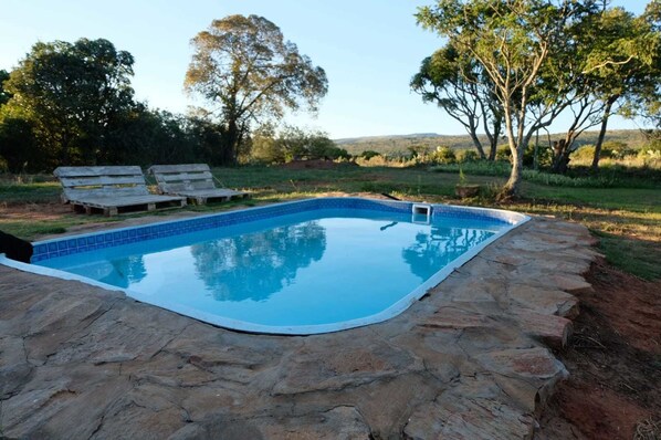 Piscina com borda de pedra, cercada por gramado e árvores.
