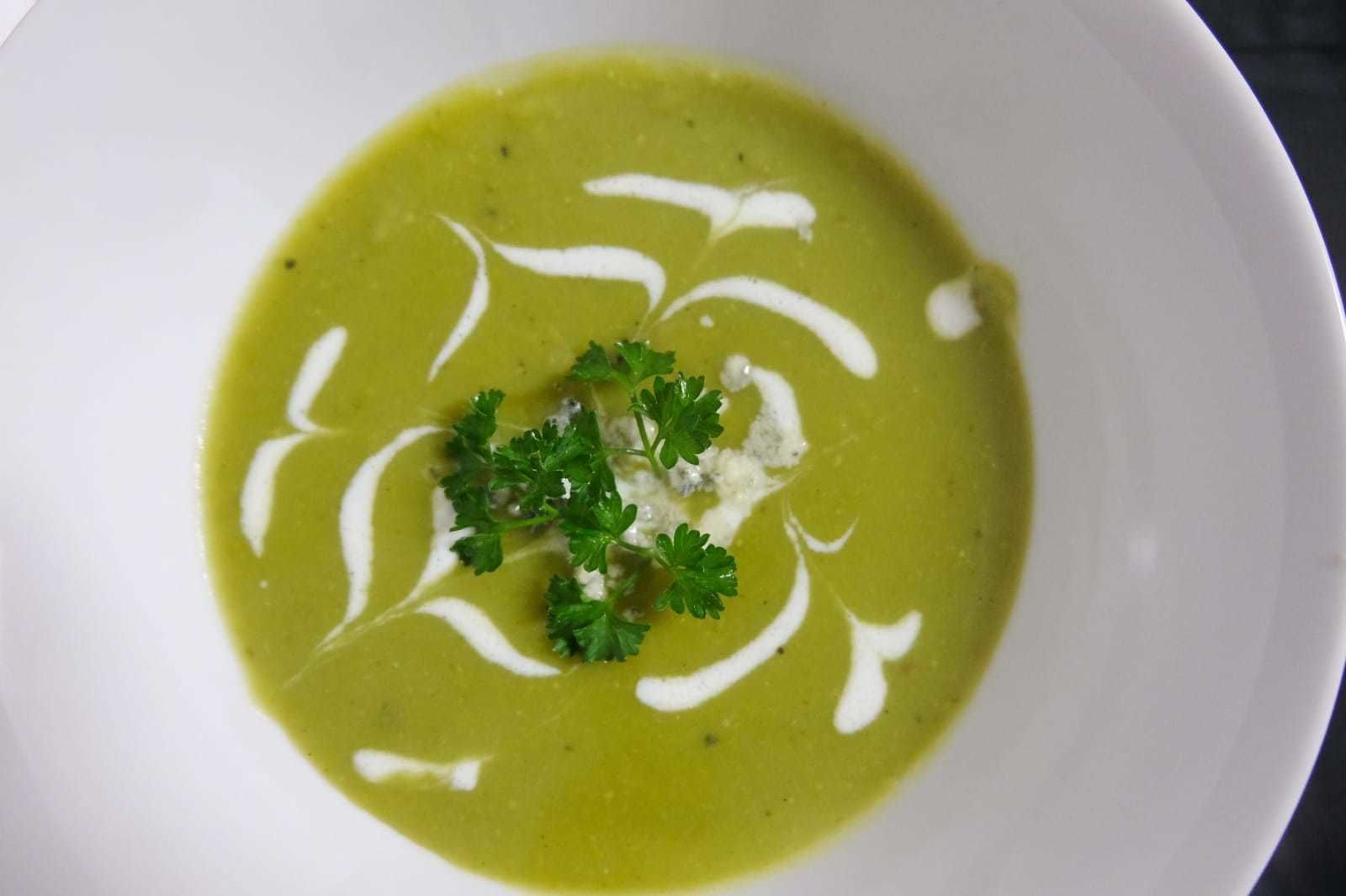 A bowl of green soup with white cream swirls and a garnish of parsley.