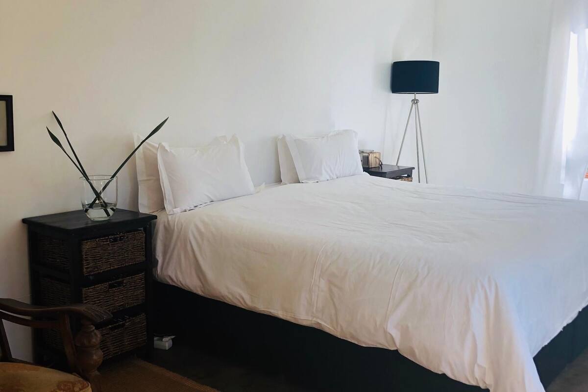 Ett sovrum med en stor säng, ett sängbord, en lampa och en vägghylla med dekorativa föremål.