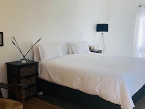 Un dormitorio con una cama grande, una mesita de noche, una lámpara y un estante en la pared con adornos.