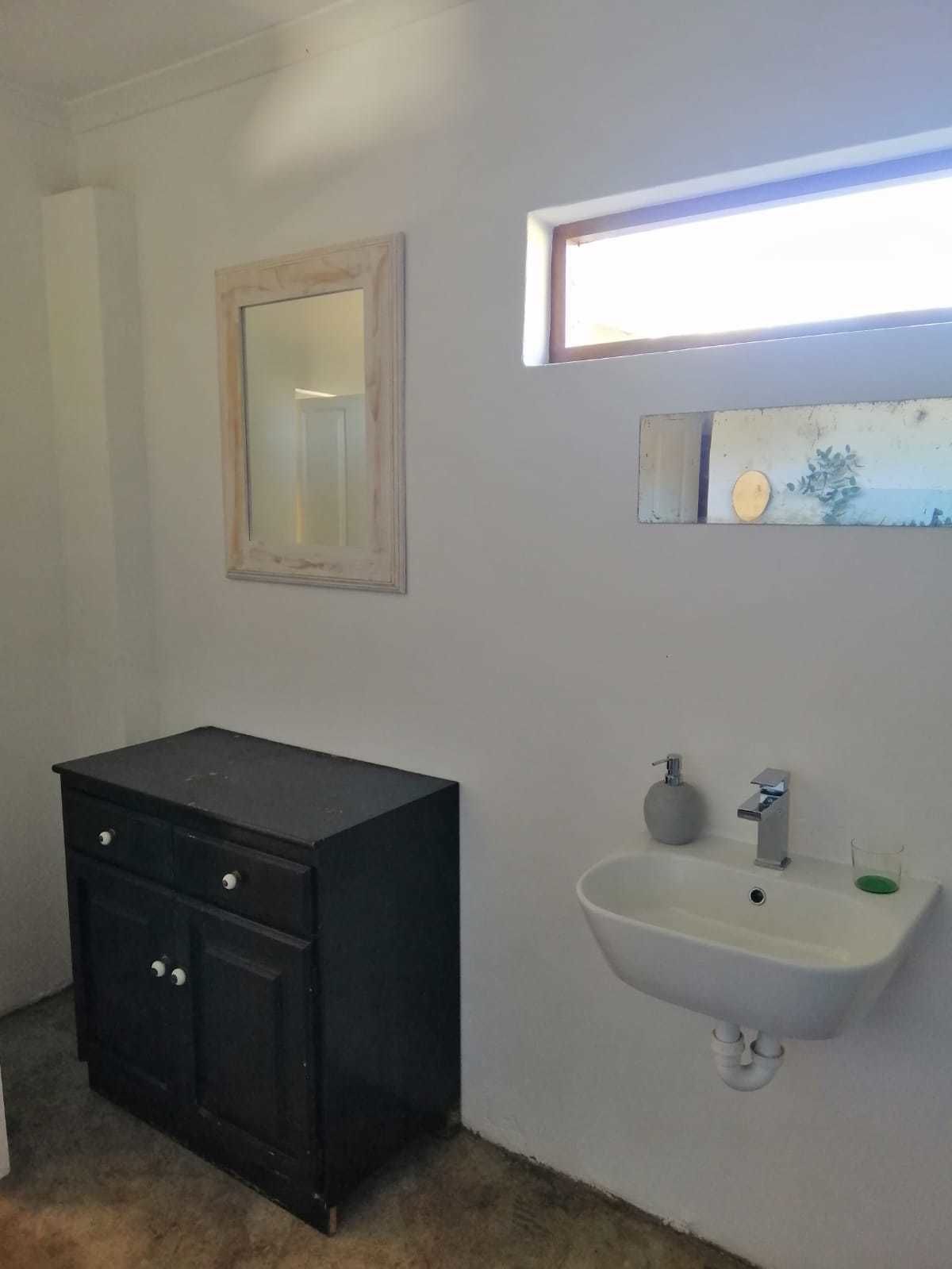 A bathroom with a black cabinet, a white sink, a mirror, and a window with daylight.