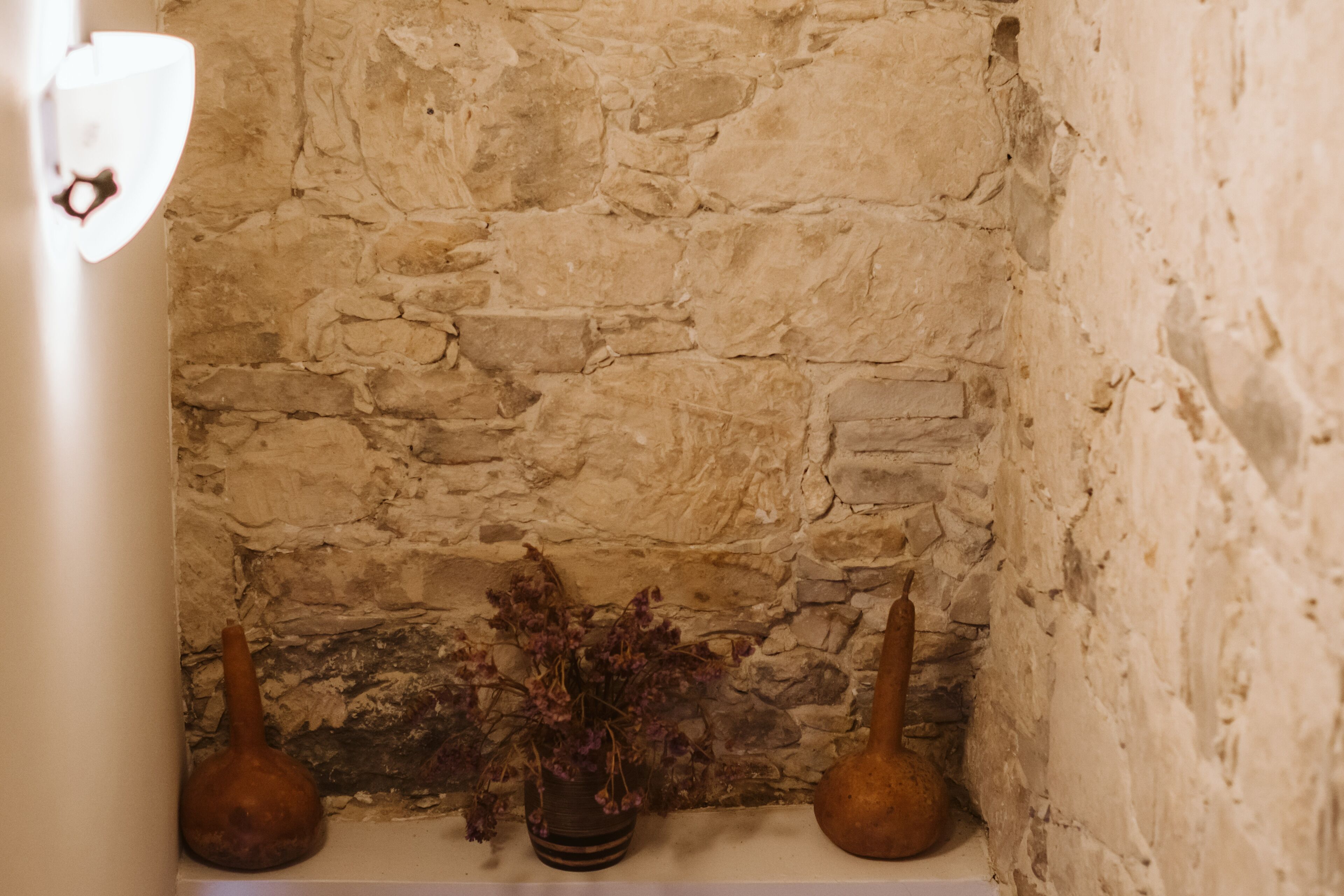 Una pared de piedra con dos jarrones y una planta en maceta sobre un estante.
