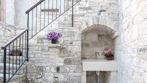 A stone staircase with a metal railing, a small sink with a potted plant, and a window with flowers. - Ariadni Gaia Cottage (Limassol)