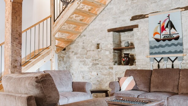 A rustic interior with exposed wooden beams, a stone wall, and a staircase leading to an upper level. - Ariadni Gaia Cottage (Limassol)