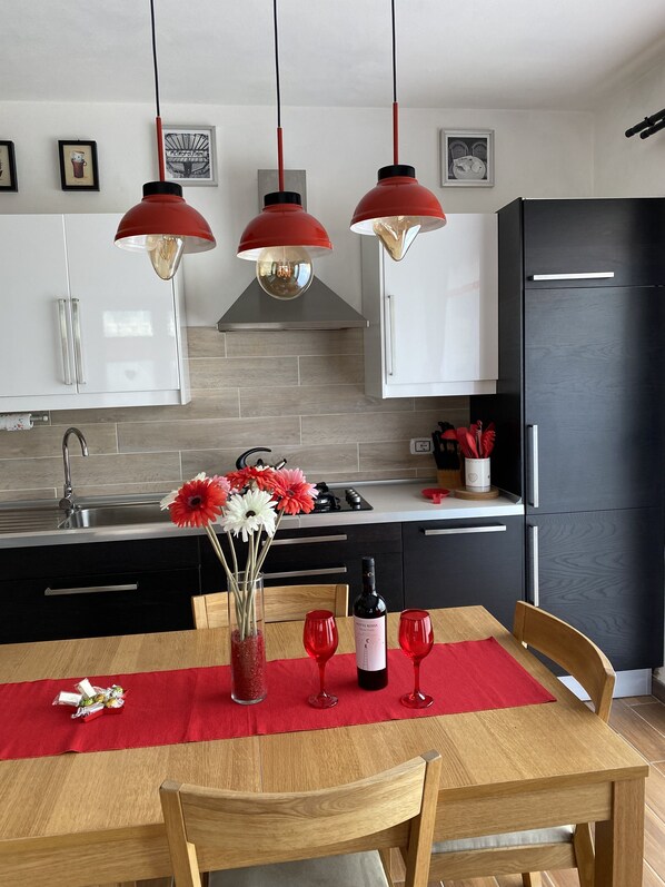 A modern kitchen with white cabinets, a black refrigerator, and red pendant lights.