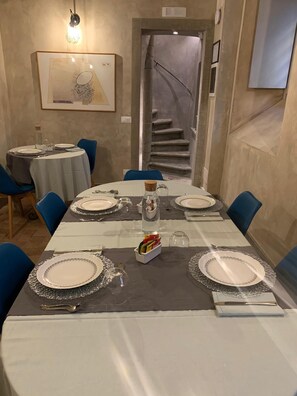 A dining area with a long table set for a meal, blue chairs, and a staircase in the background. - Santa Caterina Relais (Rome)