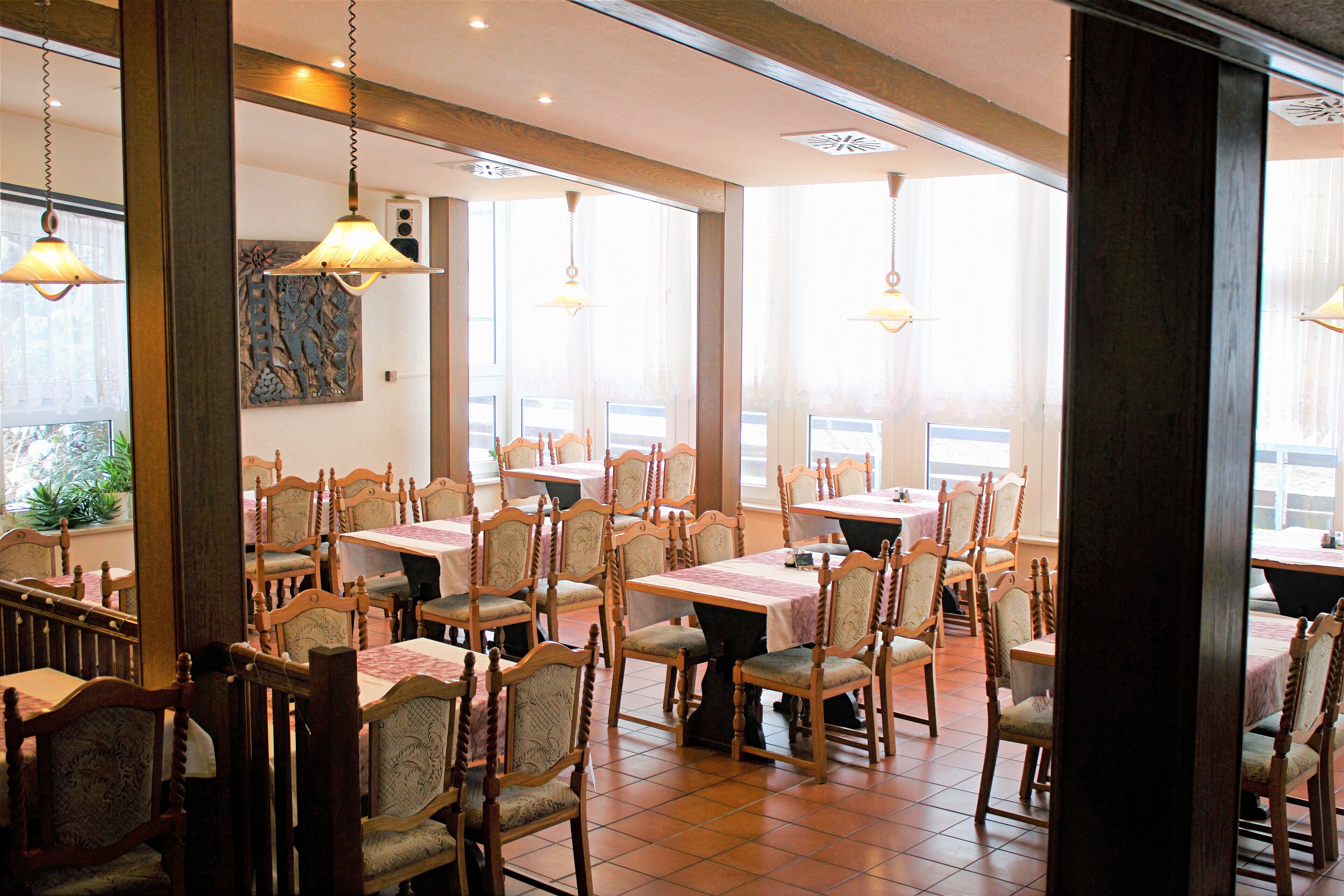 Un restaurante con sillas y mesas de madera, ventanas amplias y lámparas colgantes.