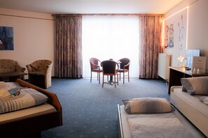Une chambre d’hôtel avec un lit, un bureau, une chaise, une table et une fenêtre avec des rideaux.