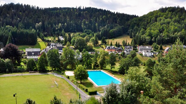 A residential area with a swimming pool surrounded by houses and greenery. - Waldhotel Feldbachtal (Neuhaus am Rennweg)