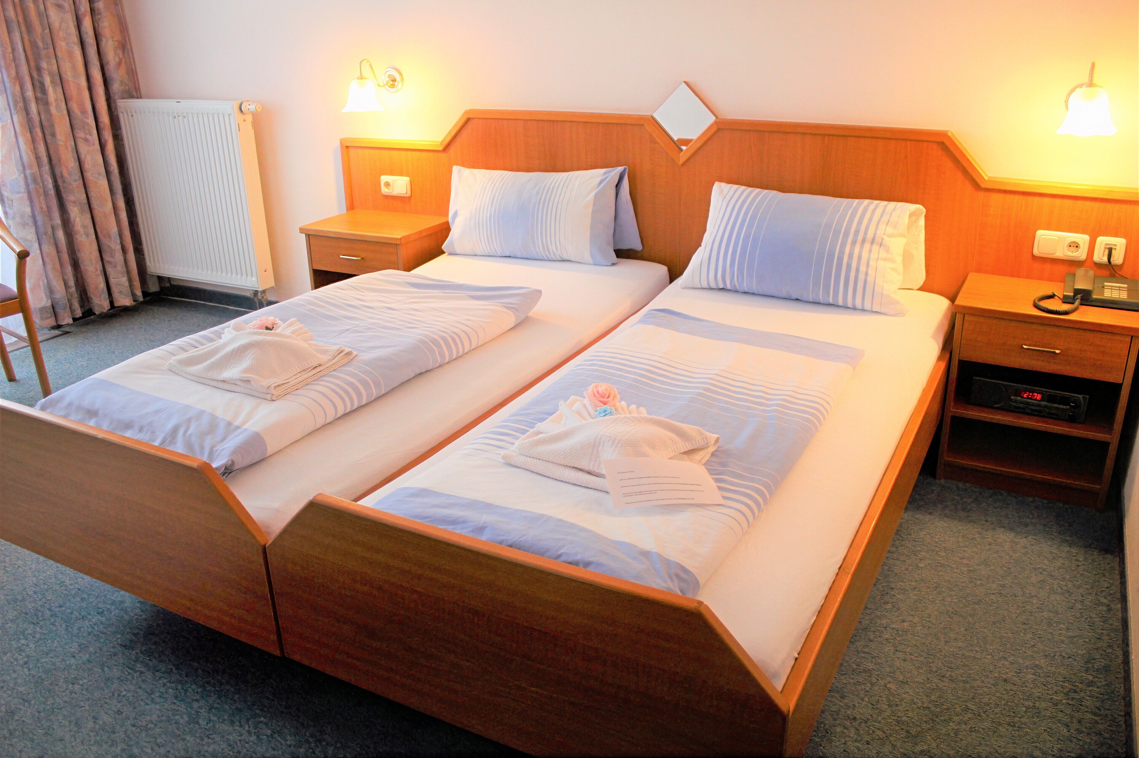 A double bed with a wooden headboard, two bedside tables with lamps, a radiator, and a telephone on the nightstand.
