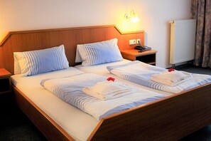 Une chambre d’hôtel avec deux lits, chacun doté de draps et d’oreillers à rayures, une table de chevet avec une lampe et un téléphone.