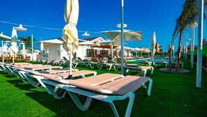 A poolside area with sun loungers, umbrellas, and a building in the background. - Camping Sol de Calpe Boreal - Caravan park (Calpe)