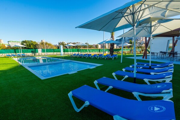 A swimming pool with blue lounge chairs and umbrellas, surrounded by green artificial grass. - Camping Sol de Calpe Boreal - Caravan park (Calpe)