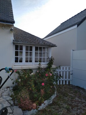 A residential property with a white exterior, a window with white frames, a white picket fence, and a garden with various plants and flowers.