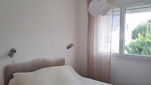 A bedroom with a bed, a window with curtains, and two wall-mounted lamps.