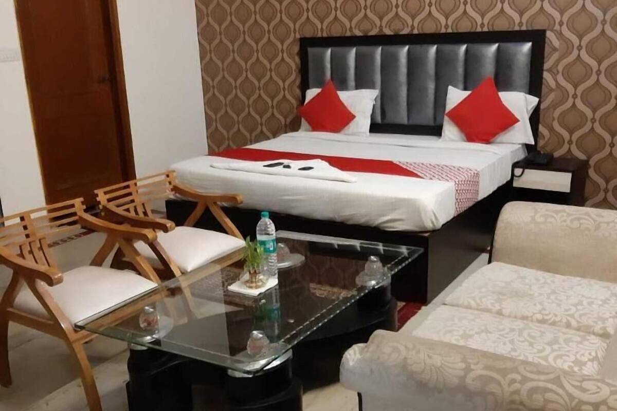 A hotel room with a bed, two wooden chairs, a glass coffee table, a sofa, and a patterned wall.