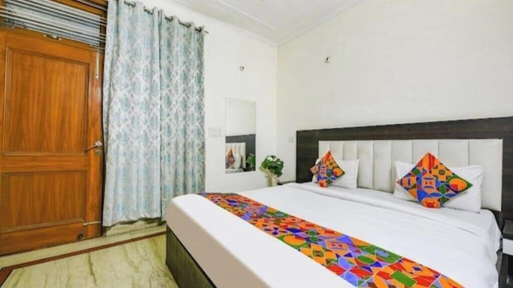 Ein Hotelzimmer mit einem Bett, einer Holztür und einem mit Vorhängen versehenen Fenster.