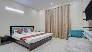 A modern bedroom with a bed, nightstand, and a teal chair. - Winsome Residency (Noida)