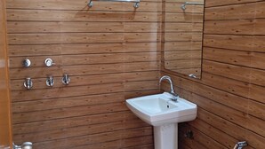 A bathroom with wooden panel walls, a white sink, a handheld showerhead, and a toilet. - Winsome Residency (Noida)