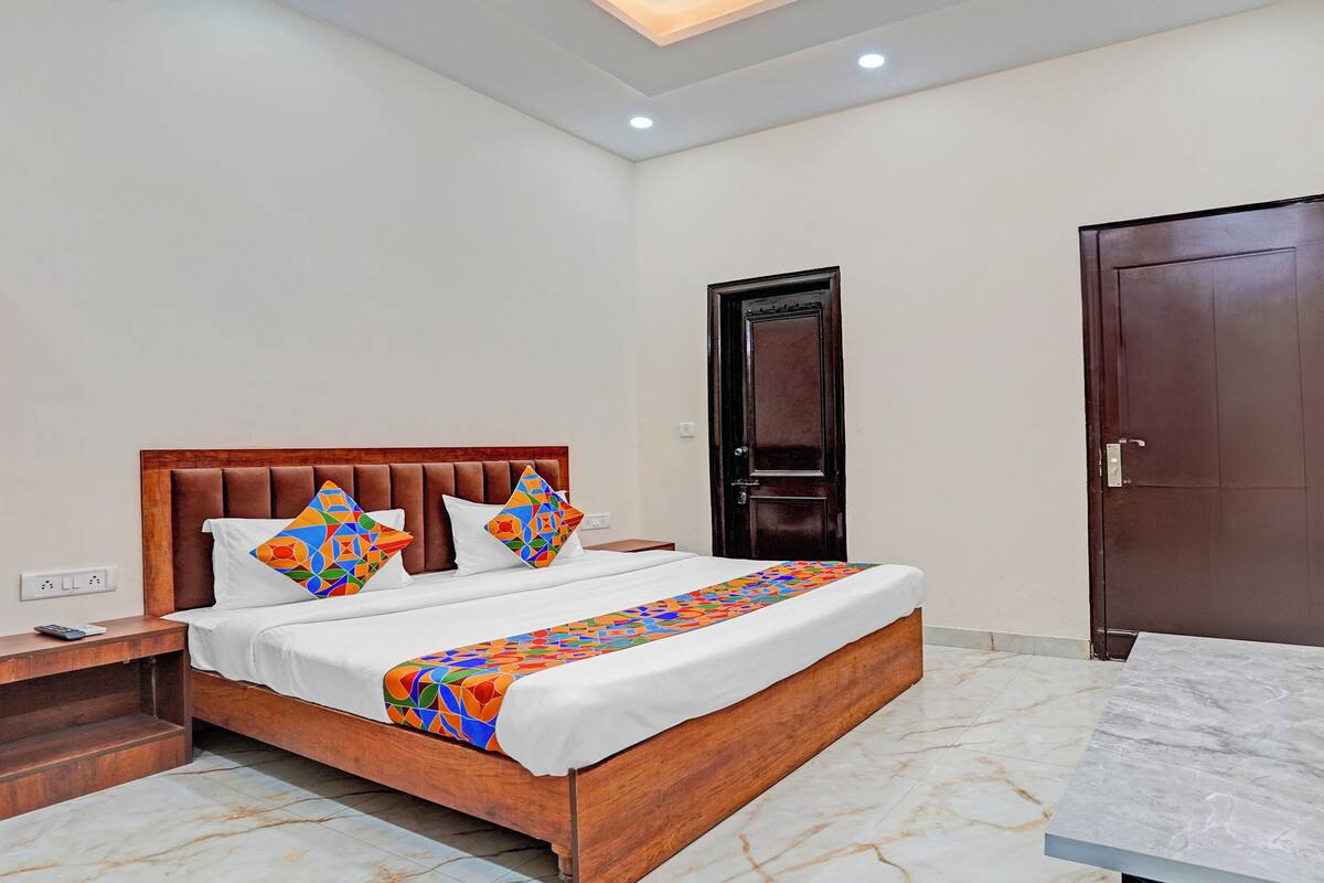 A hotel room with a bed, a wooden headboard, a nightstand, a TV mounted on the wall, and a door.