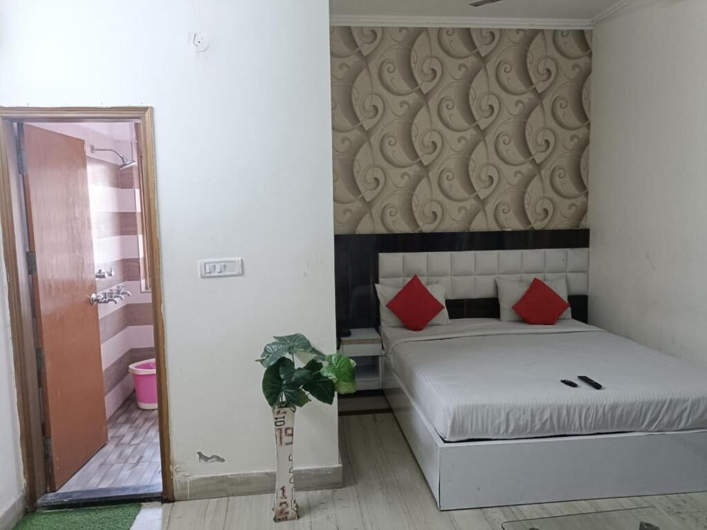 A bedroom with a bed, a decorative headboard, a potted plant, and a door leading to a bathroom.