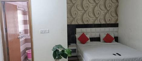 A bedroom with a bed, a decorative headboard, a potted plant, and a door leading to a bathroom.