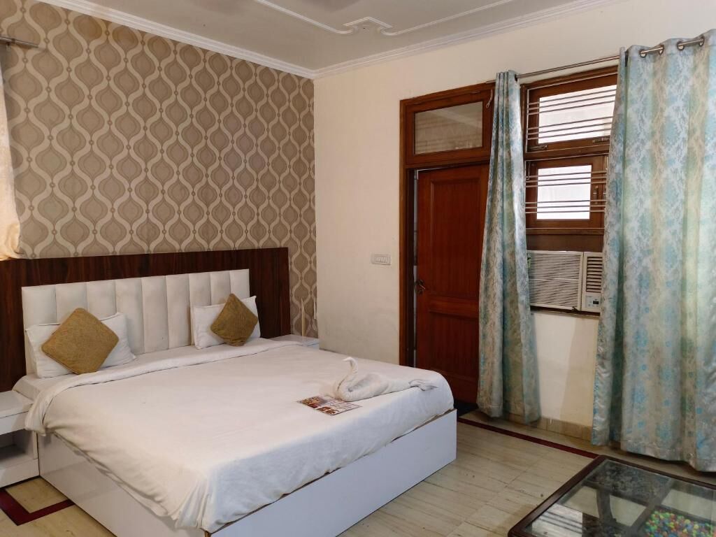 A hotel room with a bed, a wooden headboard, a window with curtains, and an air conditioning unit.