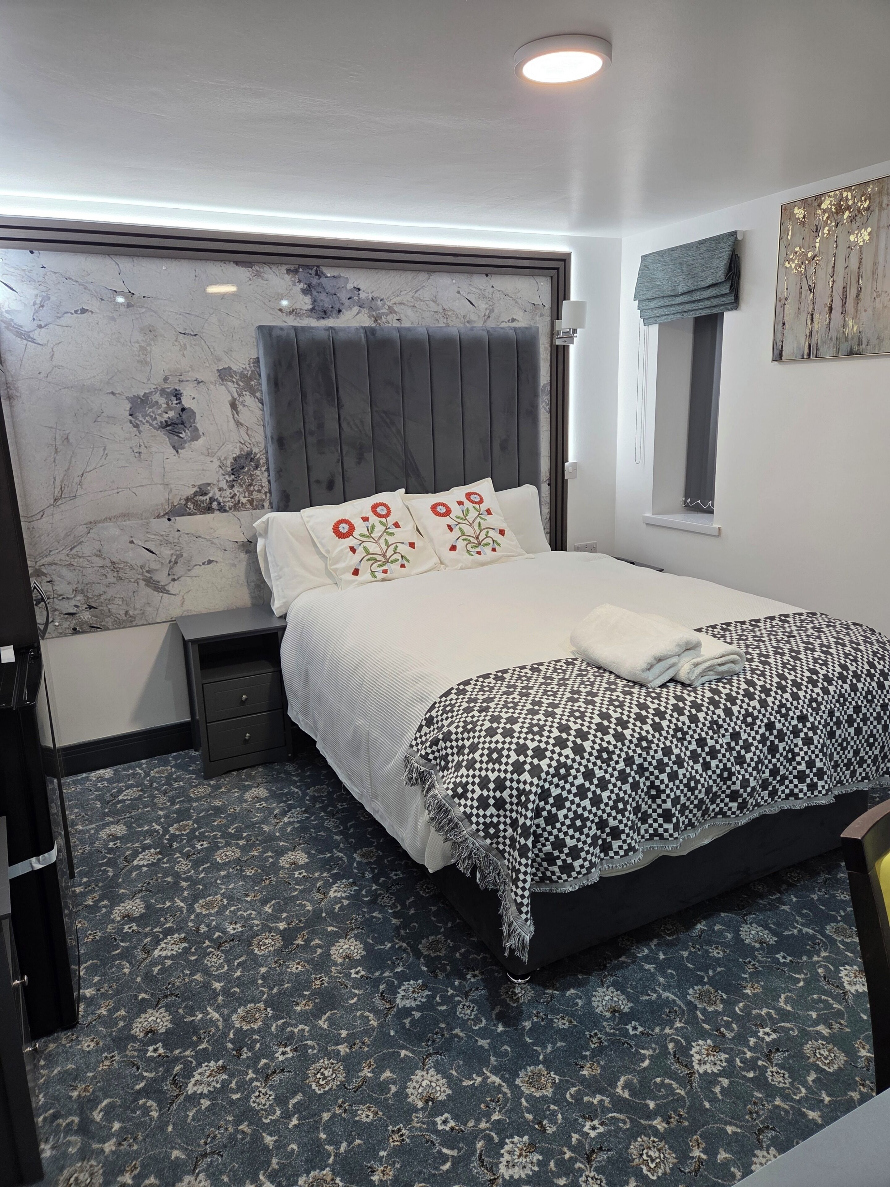A bedroom with a bed, nightstands, a marble wall, a window, and a patterned carpet.